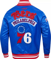 A royal blue satin Philadelphia 76ers varsity jacket shown from the back, featuring red and white stripes on the collar, cuffs, and hem, with '76ERS PHILADELPHIA' and the number '76' in red and white.