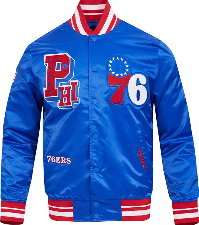 A royal blue satin varsity jacket featuring Philadelphia 76ers graphics, including a large red and white 'PHI' logo on the left chest, a red and white '76' with a star circle on the right chest, and '76ERS' embroidered on the lower left front. The jacket has red and white striped ribbed collar, cuffs, and hem, and is shown against a plain white background.