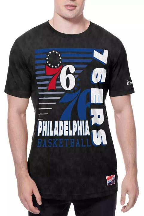 A man wearing a black Philadelphia 76ers basketball graphic t-shirt with a blue, red, and white design on the front, featuring the team logo and '76ERS' text.