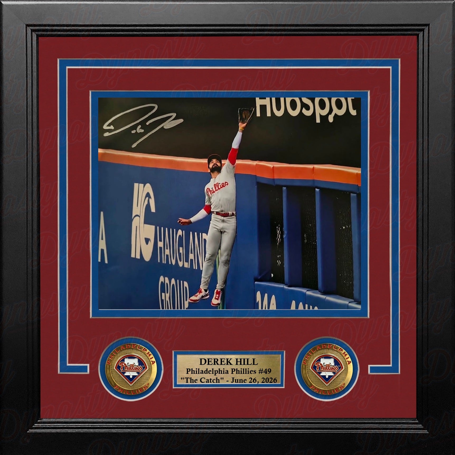 A framed 8x10 autographed baseball memorabilia print featuring Derek Hill of the Philadelphia Phillies jumping to make a catch. The piece is professionally matted with a red and blue border, set in a black frame with a custom gold nameplate and two circular team emblems.