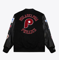 Black Philadelphia Phillies varsity jacket shown from the back, featuring a large red and white Phillies 'P' logo with 'PHILADELPHIA PHILLIES' text embroidered in red and white. The sleeves are made of black faux leather, and several team patches are visible on the sleeves.