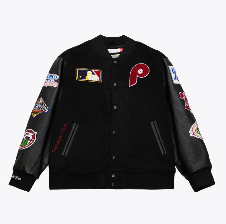 A black varsity-style baseball jacket with black leather sleeves, featuring a red Philadelphia Phillies 'P' logo on the left chest, a MLB patch on the right chest, and multiple championship patches on both sleeves.
