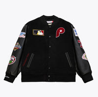 A black varsity-style baseball jacket with black leather sleeves, featuring a red Philadelphia Phillies 'P' logo on the left chest, a MLB patch on the right chest, and multiple championship patches on both sleeves.